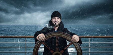 Attractive man with beard is driving the ship through rough seasの写真素材