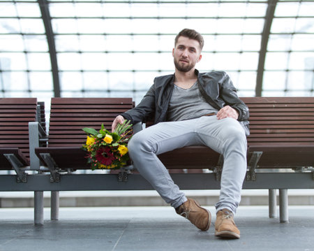 Attractive man with flowers in his hand is waiting at a train stationの写真素材