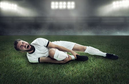 Attractive soccer player is lying on the floor and screaming and holding his legの写真素材