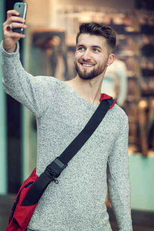 Attractive man with a beard is taking a photo of himself