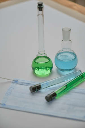 Close up vertical photo of chemistry glassware putting together on white working desk with face mask. Covid researchの写真素材