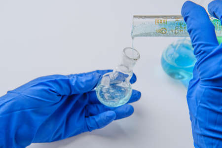 Scientist holding flask and tube at laboratory, closeup. Solution chemistry. Antivirus solution. Blue and green liquidの写真素材