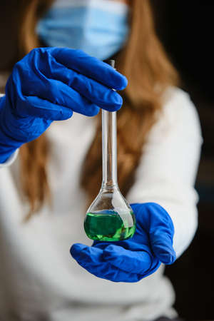 Closeup of a glass flask with green liquid. Scientist is holding up. Selective focus. virus cureの写真素材