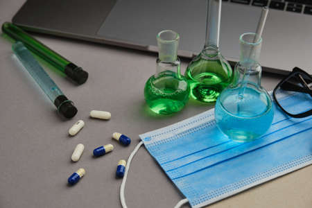 Laboratory flask with green and blue liquid and pills. Research for the virus cure and laptopの写真素材