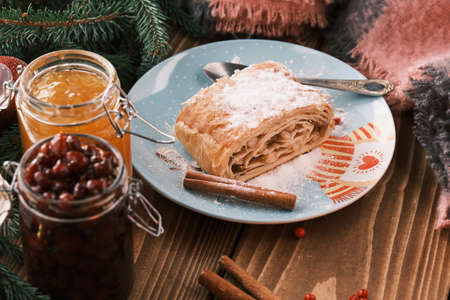 Closeup of a strudel on a Christmas plate near cinnamon sticks and a jam jars. Christmas breakfast on a wooden tableの写真素材