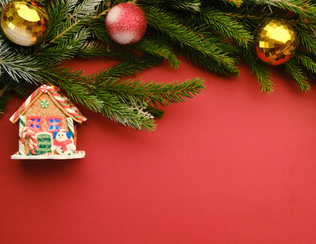 Flat lay with pine tree branches with red and golden Christmas balls isolated on red and a toy house