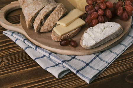 Closeup view o a wooden board with Ciabatta, grape and cheese. Sliced with creme cheeseの写真素材