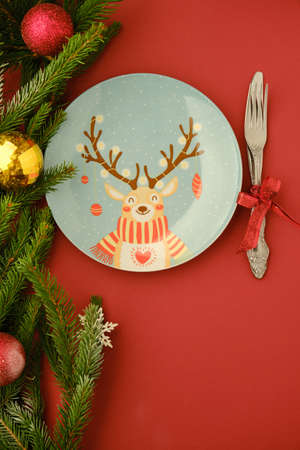 Christmas deer plate with fork and knife on a wooden background with christmas tree and toysの写真素材