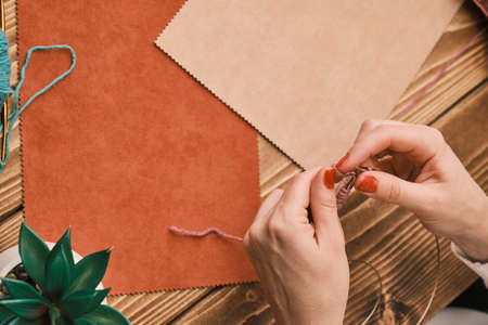 Female hands knitting doll clothes on a wooden table at home at self-quarantineの写真素材