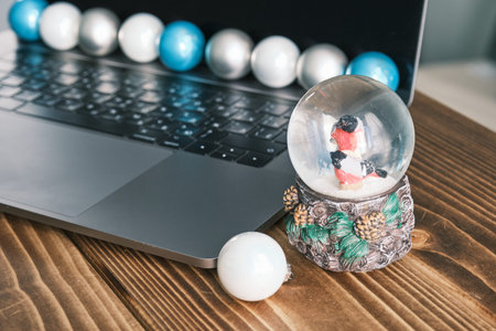Christmas work space with laptop nad Christmas toys balls on a wooden table.