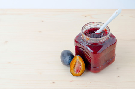 Open jar of plum jam on wooden tableの写真素材