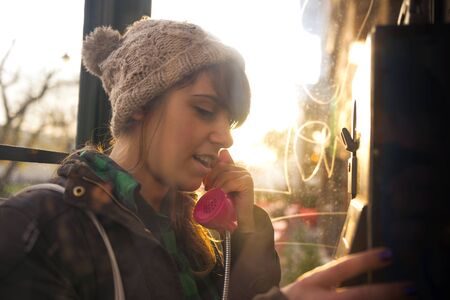 Hipster woman on the pay-phone in the city on sunny day.の写真素材