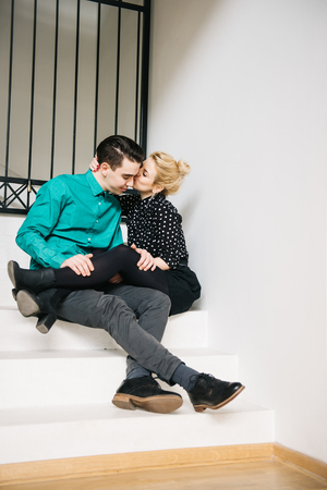Happy stylish couple sitting on the stairs in their luxurious house. Passionate kissの写真素材
