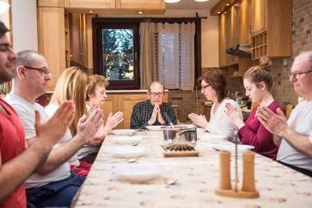 Big generation family having dinner, praying. Focus in the center of the frame on the grandpa, natural light used. Horizontal composition, narrow depth of fieldm natural lightの写真素材