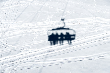 Shadow of the chairlift with four people in the snow. Direct sunlight.の写真素材