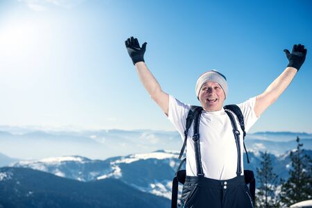 Middle aged man celebrating with raised hands his success. He just got up on the top of the mountain. Warmer highlights, lens flare into the camre. Copy space on the left of the frame, shallow depth of field.の写真素材