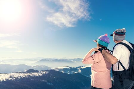 Middle aged couple on the top of the mountain looking away. Direct sunlight, lens flare, warmer tones on highlights. A lot of copy space on the left side of the frame.の写真素材