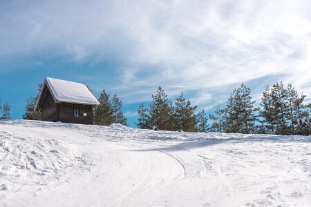 Small wooden house on he mountain covered with snow, Direct sunlight with lens flare from the right side of the frame. Copy spaceの写真素材