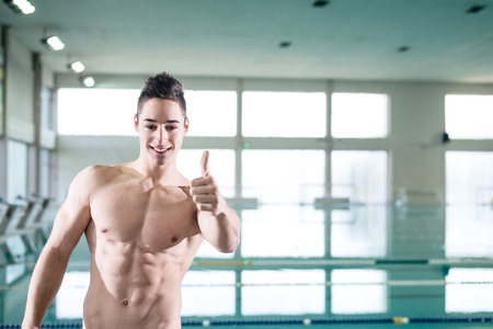 Young muscular man gesturing thumb up by the pool at leisure centerの写真素材