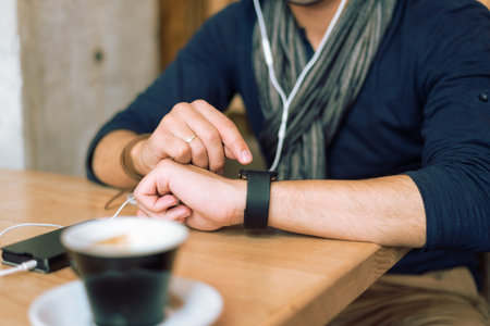 Young stylish and fashionable man checking his smartwatch in cafe bar. High angle shot. Selective...