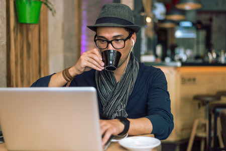 Fashionable and stylish young man drinking coffee, listening music and internet browsing at the cafe bar. Selective focus. Toned image.の写真素材
