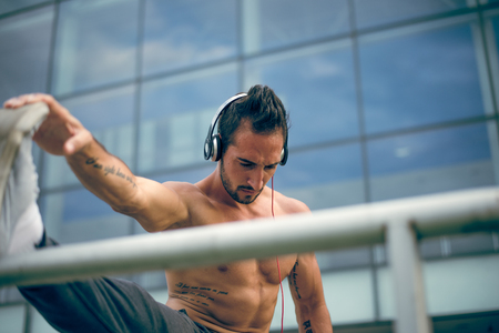Young man listening to the music and stretching his leg after a heavy workout. Wearing tracksuits without shirt. Selective focus.の写真素材