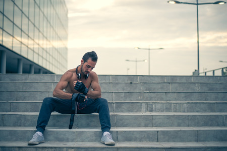 Young male prepering for hard workout and putting his gloves for training. Wearing tracksuit without shirt. In the backgroung modern sport centar. Selective focus.の写真素材