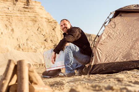 Middle aged motorcyclist relaxing after a long ride on motorbike. Checking his travel map in tent. Lens flare. Warm colors.の写真素材