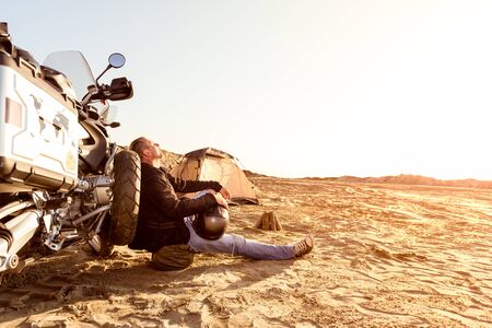 Middle aged motorcyclist relaxing after a long ride on motorbike. Lens flare. Warm colors. Selective focus.の写真素材