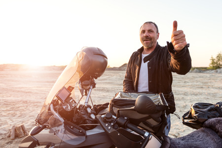 Middle aged motorcyclist won the toughest Dakar adventure. Thumbs up. Selective focus, Toned image. Lens flareの写真素材