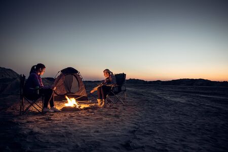 Two young girls lighting a fire in front of the tent and a sky full of stars.の写真素材