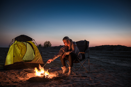 Young girl lighting a fire in front of the tent and a sky full of stars.の写真素材