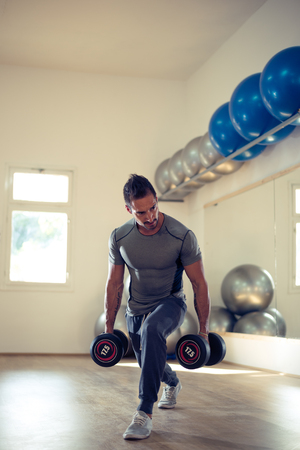 Young attractive man holding dumbbells. Selective focus. Soft focus on the face.の写真素材