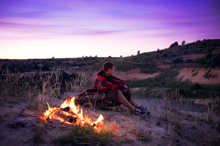 Shot of a hiker at the dawn sitting near the camping fire. High ISO, grainy image.
