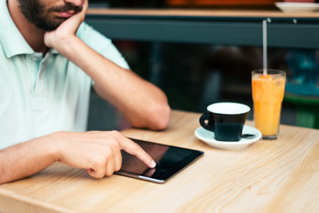 A young man working on a digital tablet in a restaurant. Natural light, Selective focus.