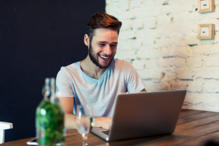 Shot of a young man working on a laptop in a cafe. Selective focus, natural light, higer ISO, grainy...