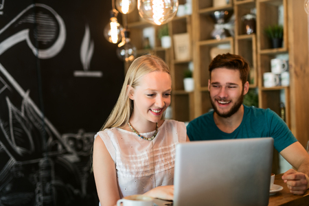 Young smiling couple working together on a laptop at a cafe shop. Selective focus, natural light.のeditorial素材