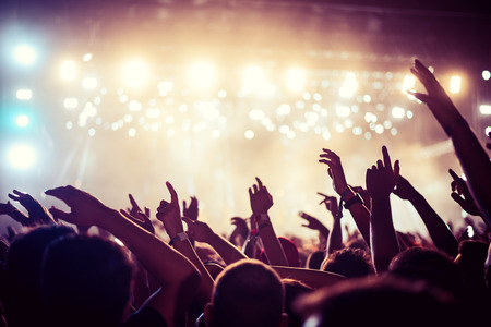 Audience with hands raised at a music festival and lights streaming down from above the stage. Soft focus, high ISO, grainy image.の写真素材