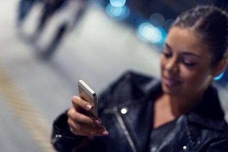Young smiling woman texting on her mobile phone. High ISO image, selective focus on the phone, narrow depth of field.の写真素材