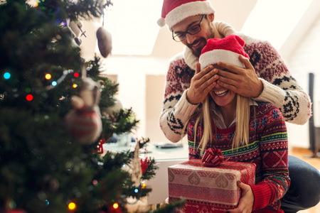 Cropped shot of a man surprising his girlfriend with a Christmas gift.の写真素材