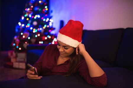 Portrait of a pretty woman in a santa hat using her mobile phone. High ISO image.の写真素材