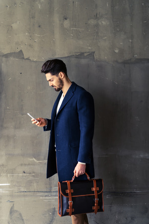 A handsome businessman using his smartphone while heading up to the office.の写真素材