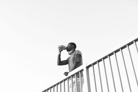 Cropped shot of a young runner standing on the bridge and drinking water.