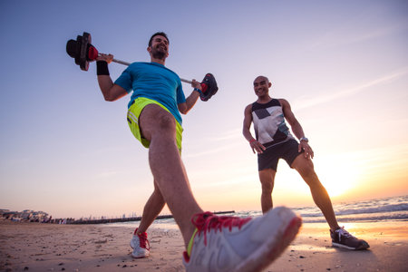 Man exercising outdoors on the beach with personal trainer