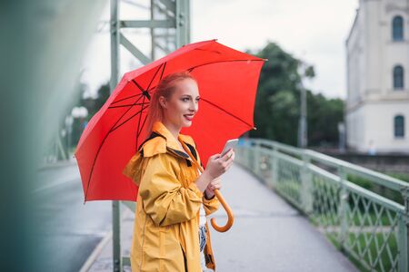 Attractive woman texting outdoors on a rainy day.の写真素材