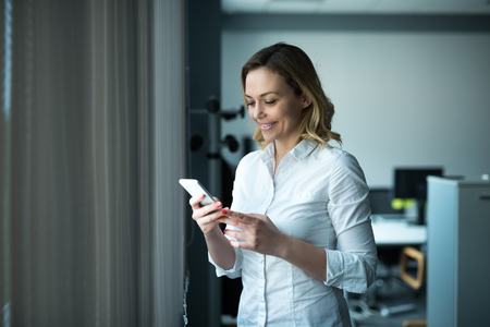 Businesswoman texting on a mobile phone in an office.の写真素材
