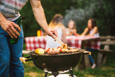Close up of a man making barbecue and holding beer bottle.の写真素材