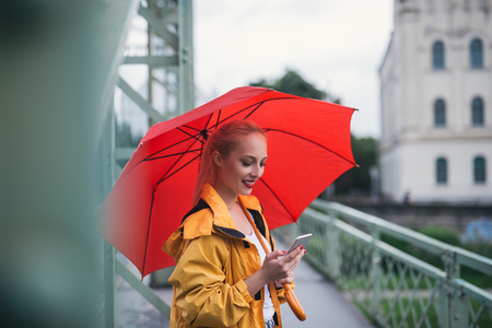 Young girl texting while walking outdoors on a rainny day.の写真素材