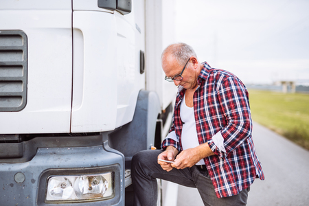 Senior driver texting on a mobile phone next to truck outdoors.の写真素材