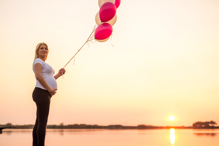 Pregnant woman holding her belly and  balloons on a sunset.の写真素材